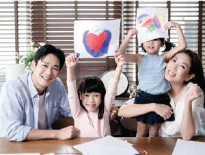 una pareja de joven con sus dos niñas mostrando dibujos de corazón