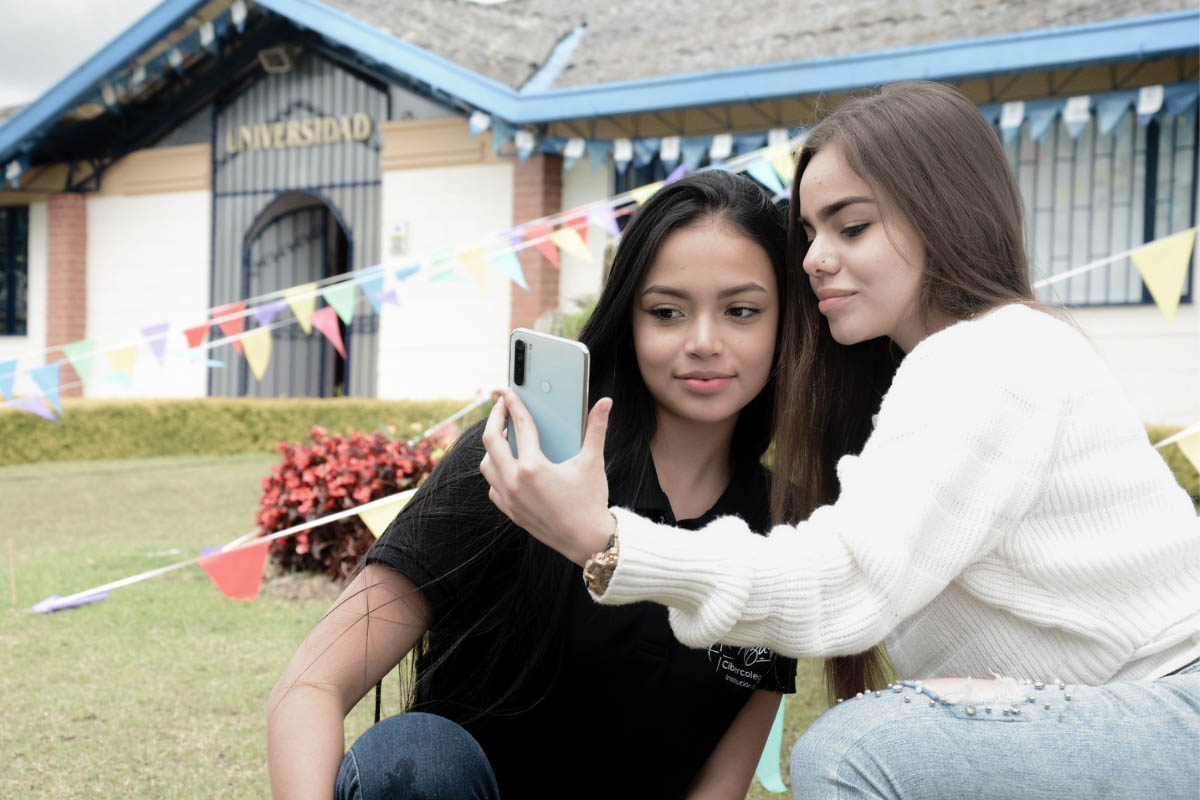 Dos mujeres jóvenes mirando el periódico escolar del Cibercolegio en su celular.