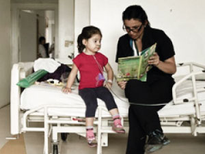 Fotografía de una niña hospitalizada y una mujer adulta leyendole un libro